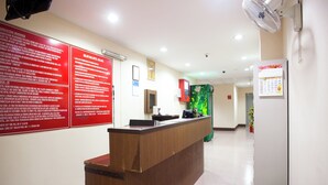 A hotel reception area with a wooden reception desk, a red informational board, a green vending machine, and a calendar on the wall. - Hotel O Melintang Hotel (Hutan Melintang)