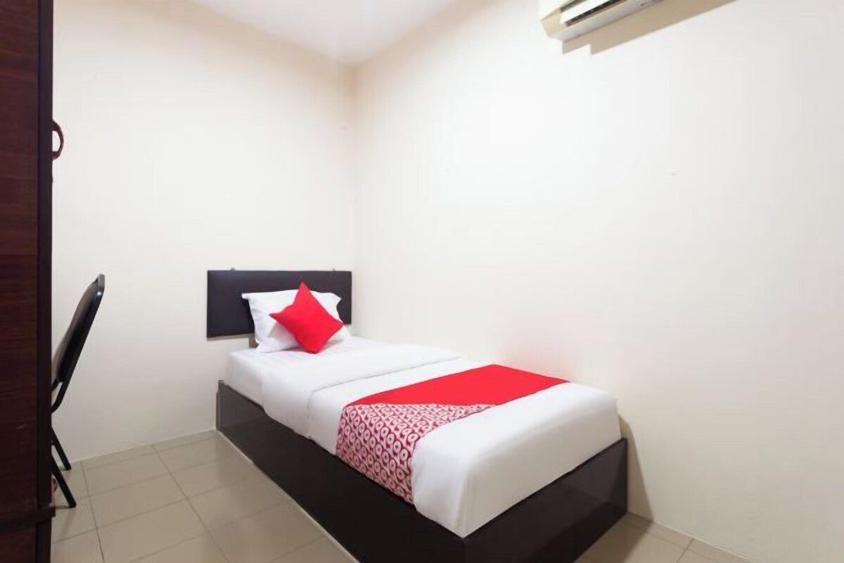 A small, neatly arranged bedroom with a single bed, a chair, and a wall-mounted air conditioning unit.
