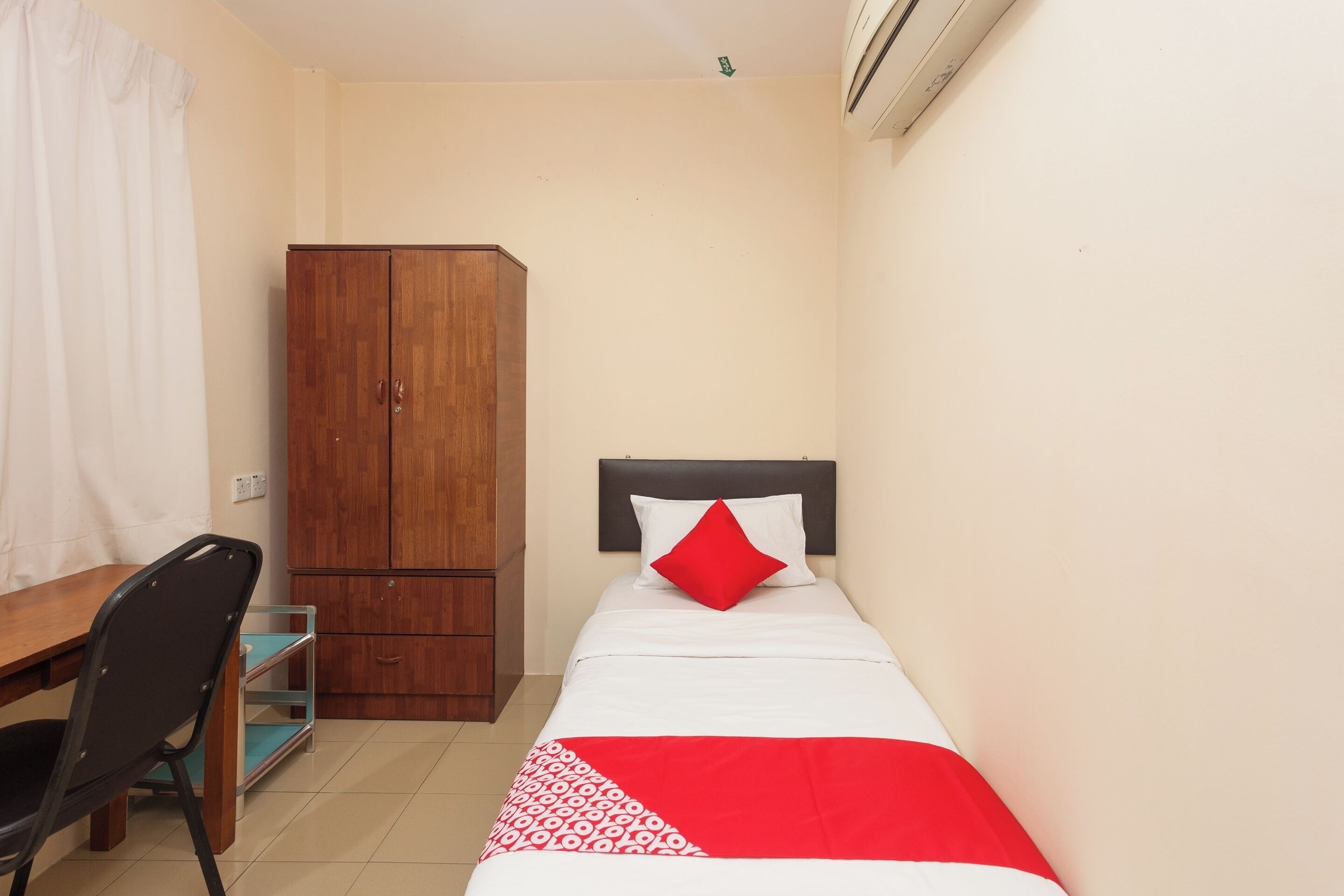 Une petite chambre à coucher, bien rangée, avec un lit simple, une armoire en bois, un bureau avec une chaise et une fenêtre avec des rideaux.