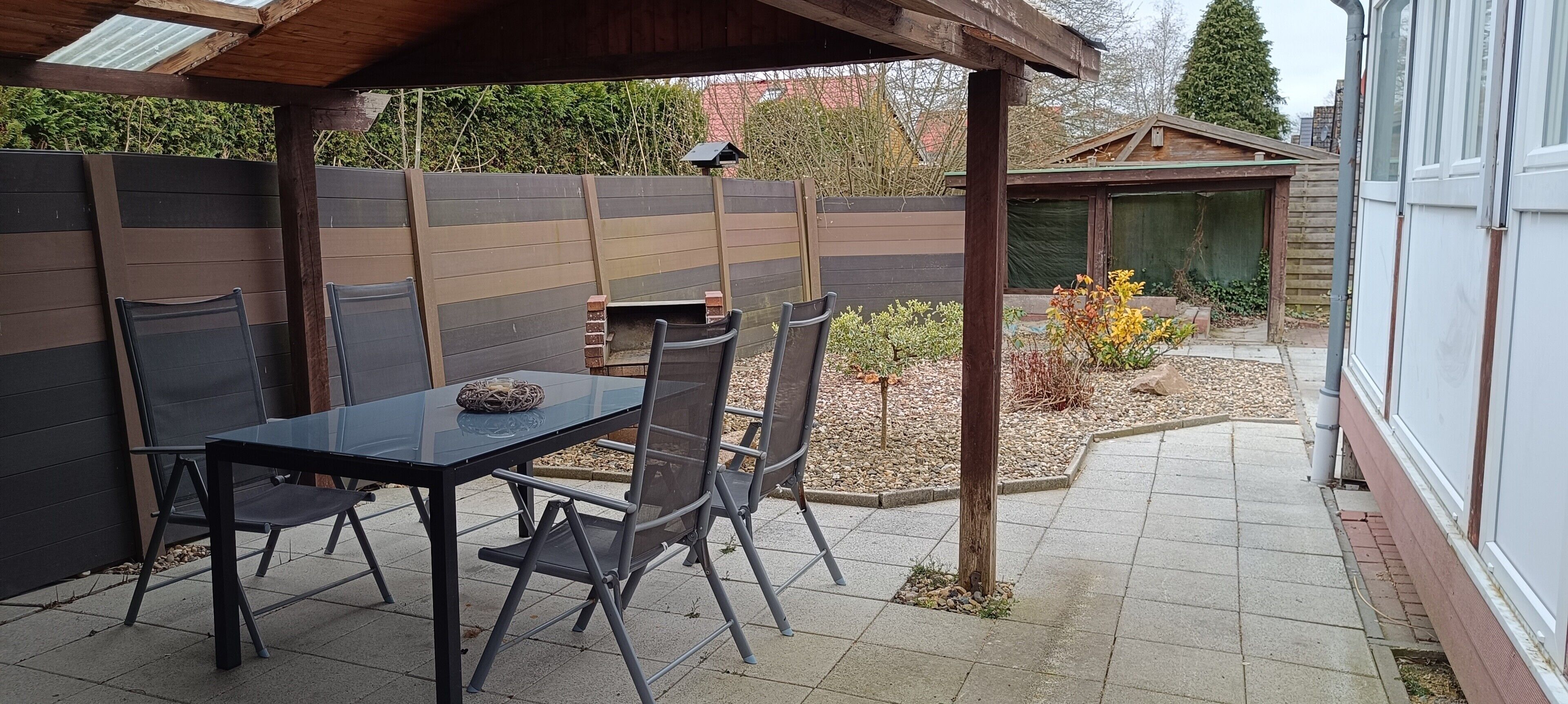 Eine Terrasse im Freien mit Tisch und Stühlen, einem Holzzaun und einem kleinen Gartenbereich.
