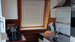 A compact kitchen with wooden cabinets, a window with blinds, a sink, and a coffee maker. - Holiday Home 'Ferienhaus Stamer Am Großen Meer' with Shared Terrace and Private Garden (Bedekaspel)