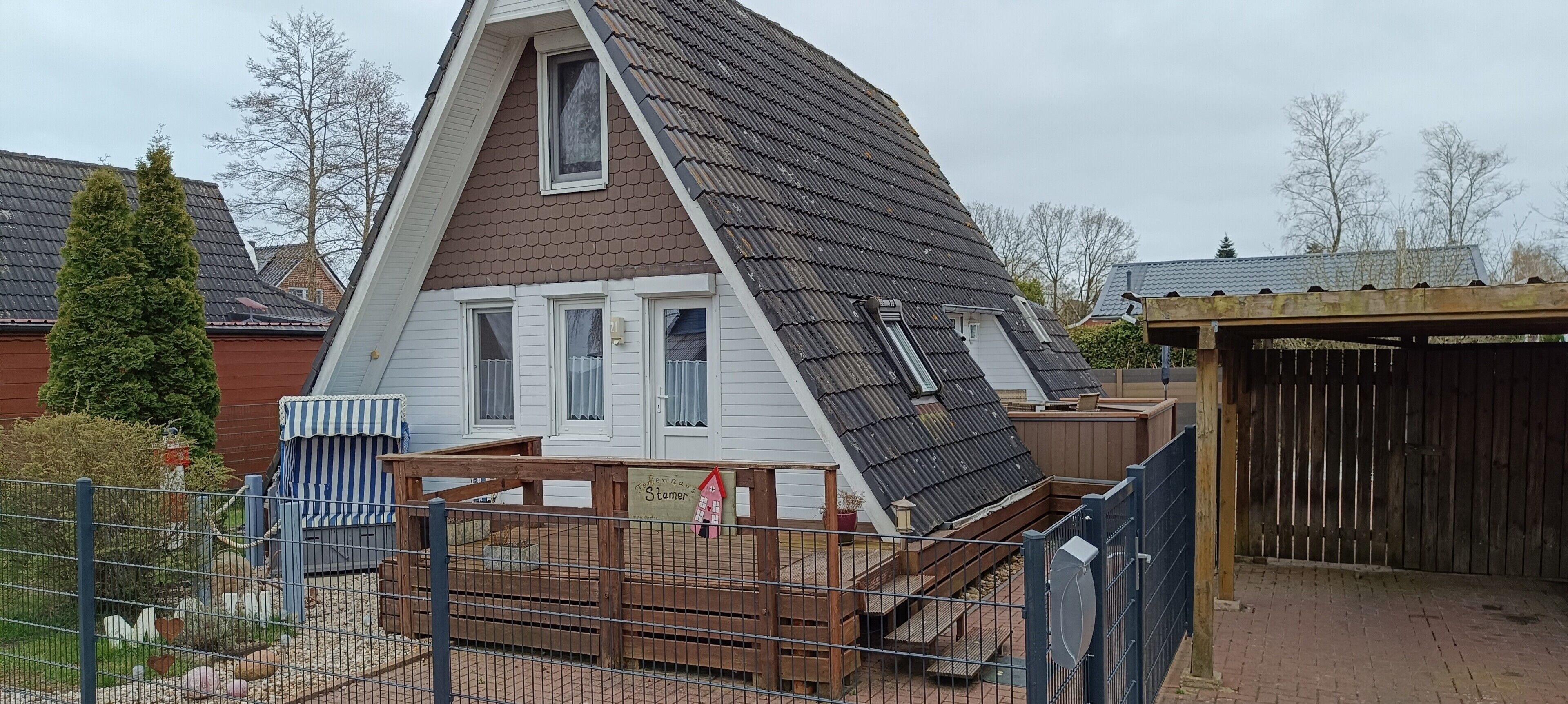 Ein Haus mit einem steilen Satteldach, Dachgauben und einem umzäunten Garten.