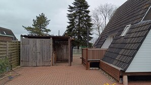 A backyard with a wooden shed, a metal roofed structure, and a white building with a slanted roof. - Holiday Home 'Ferienhaus Stamer Am Großen Meer' with Shared Terrace and Private Garden (Bedekaspel)