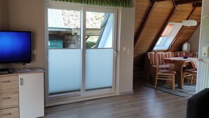 A room with a television, a sliding door, a dining area with chairs, and a wooden ceiling. - Holiday Home 'Ferienhaus Stamer Am Großen Meer' with Shared Terrace and Private Garden (Bedekaspel)