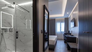 A modern hotel room with a glass-enclosed shower, a large mirror, a bed, a desk, and a TV mounted on the wall. - Hotel Leflet Sanlúcar (Sanlucar la Mayor)