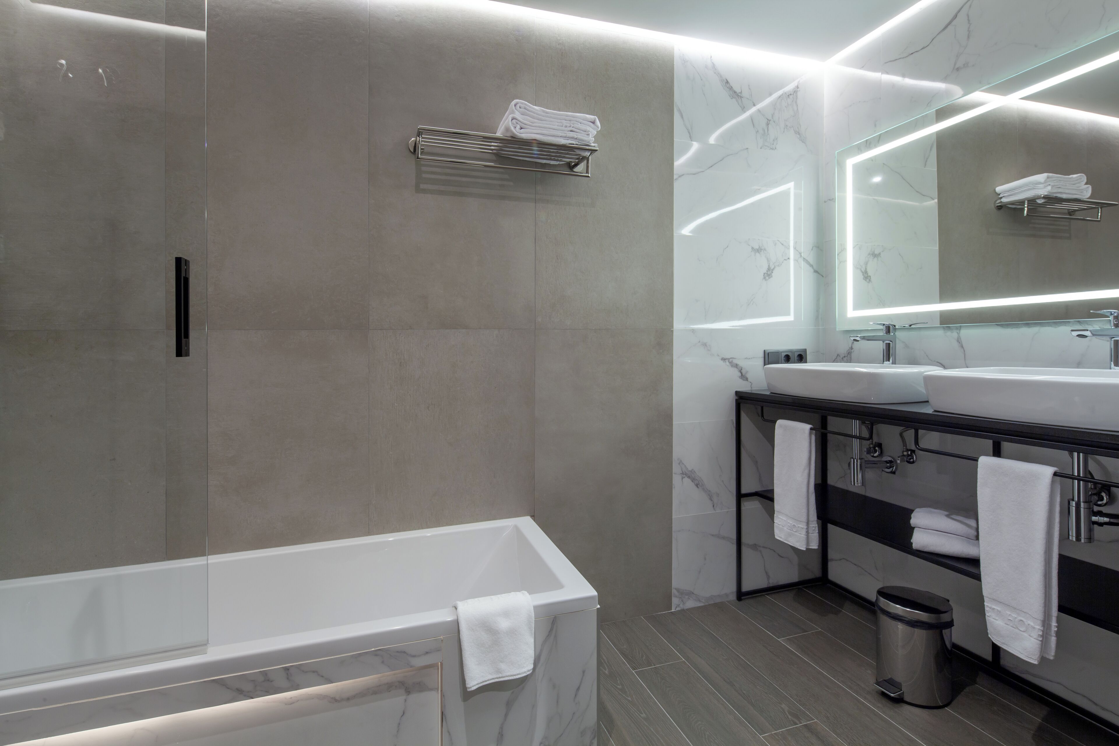 A modern bathroom with a bathtub, two sinks, a large mirror, and a towel rack.