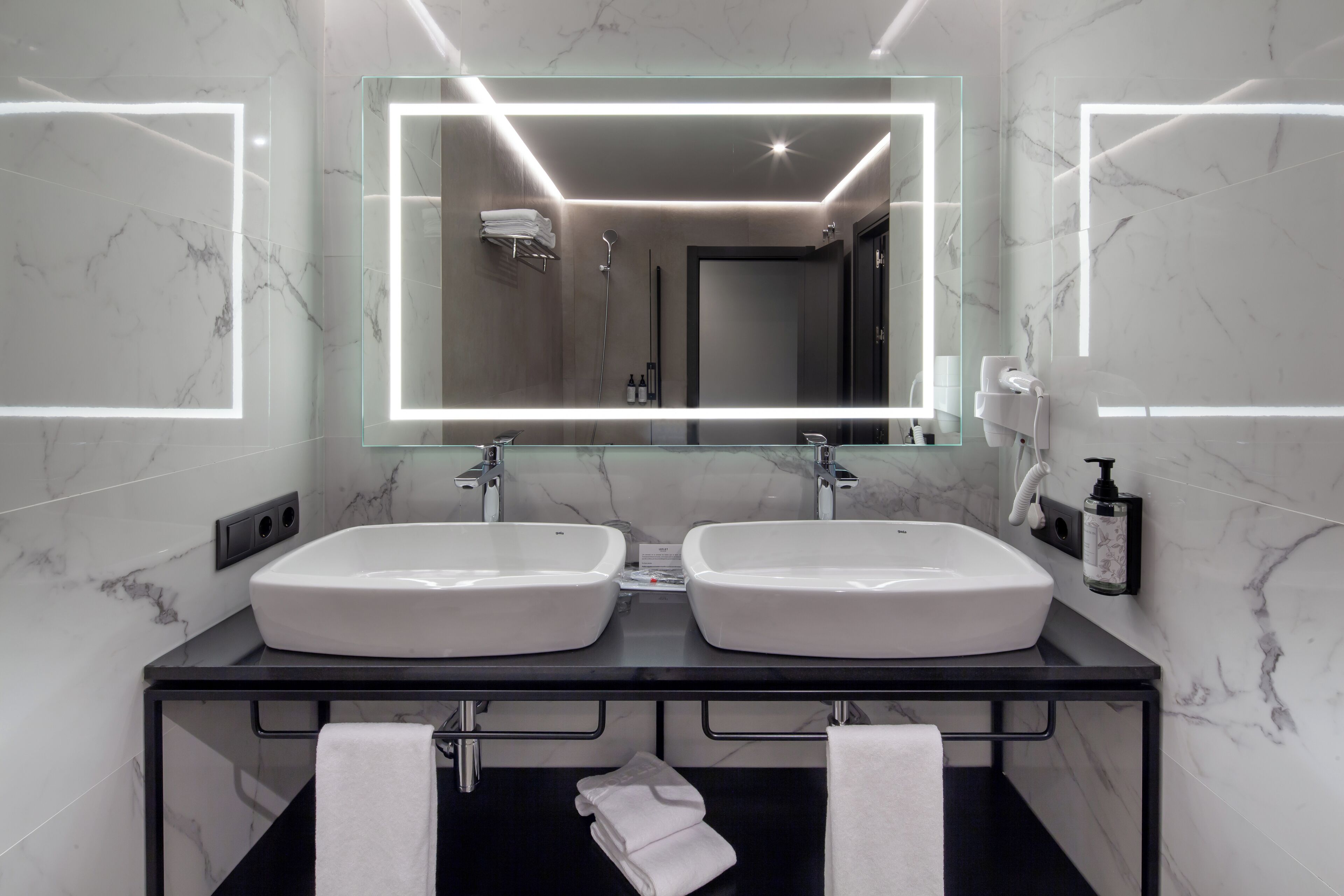 Une salle de bain moderne avec deux vasques, un grand miroir et un plan de toilette noir.