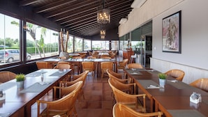 A spacious dining area with wooden tables and chairs, large windows, and a ceiling with exposed beams. - Hotel Leflet Sanlúcar (Sanlucar la Mayor)