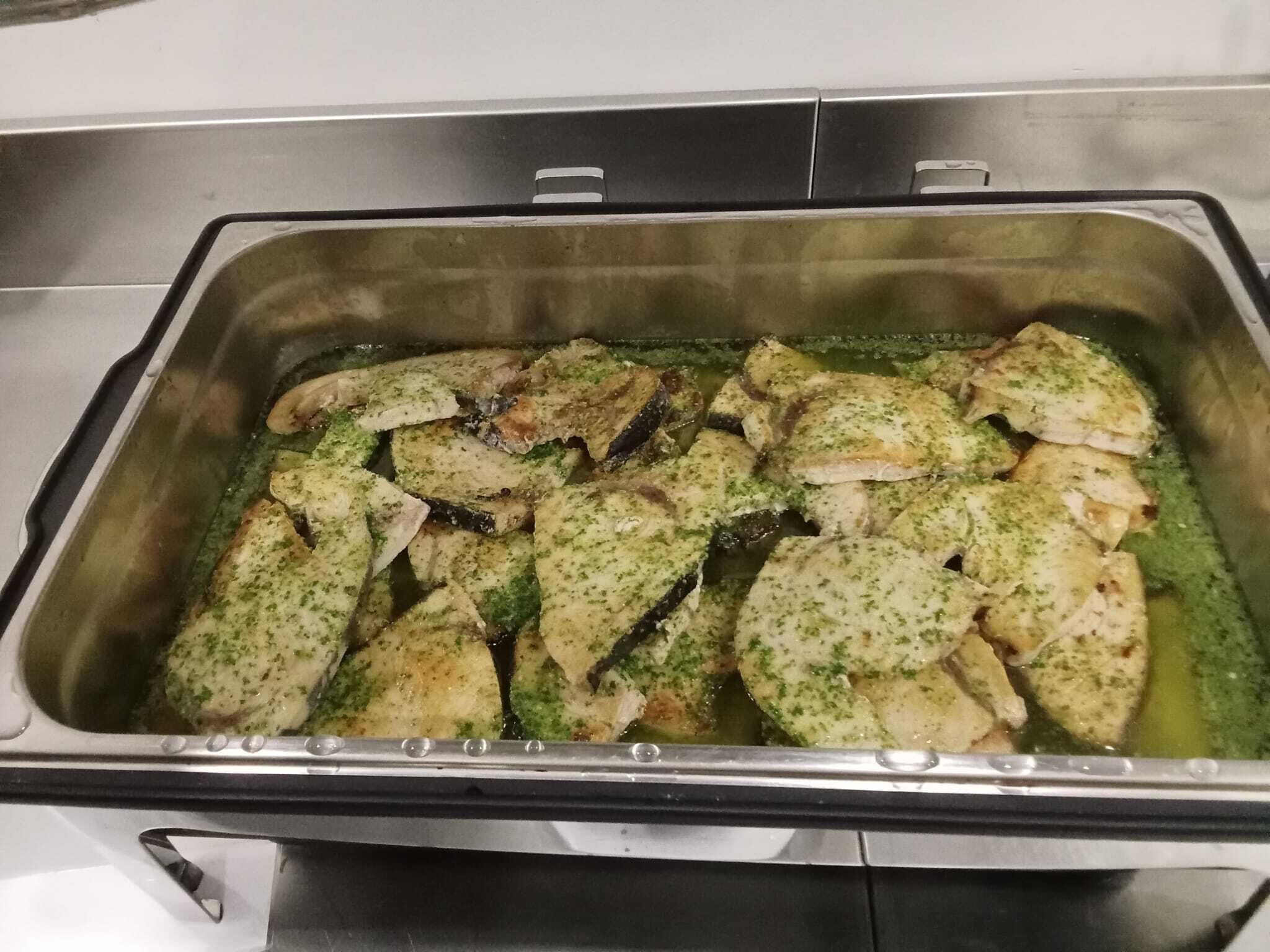 A stainless steel buffet sink with food items, including fish and vegetables, being washed.