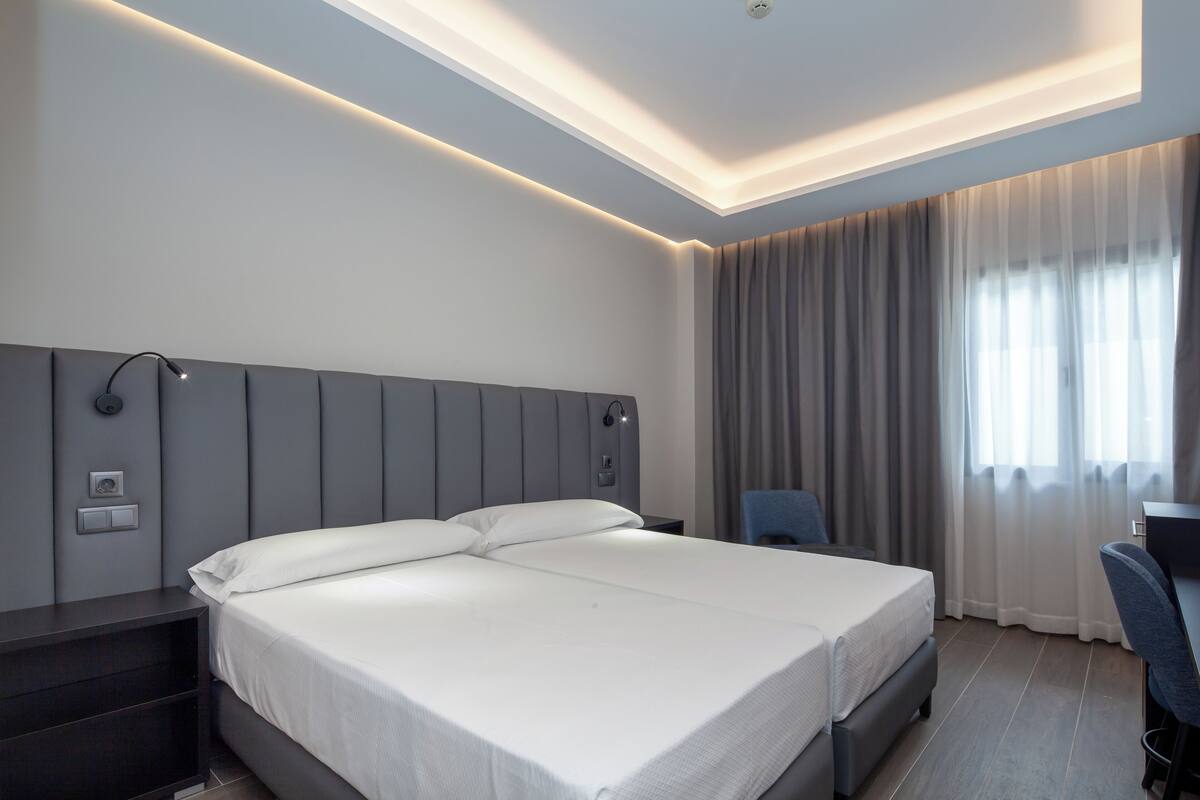 Una habitación de hotel moderna con una cama grande, mesitas de noche, un escritorio y una silla.