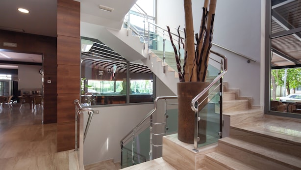 A modern interior with a staircase, glass railings, and a decorative vase with branches. - Hotel Leflet Sanlúcar (Sanlucar la Mayor)