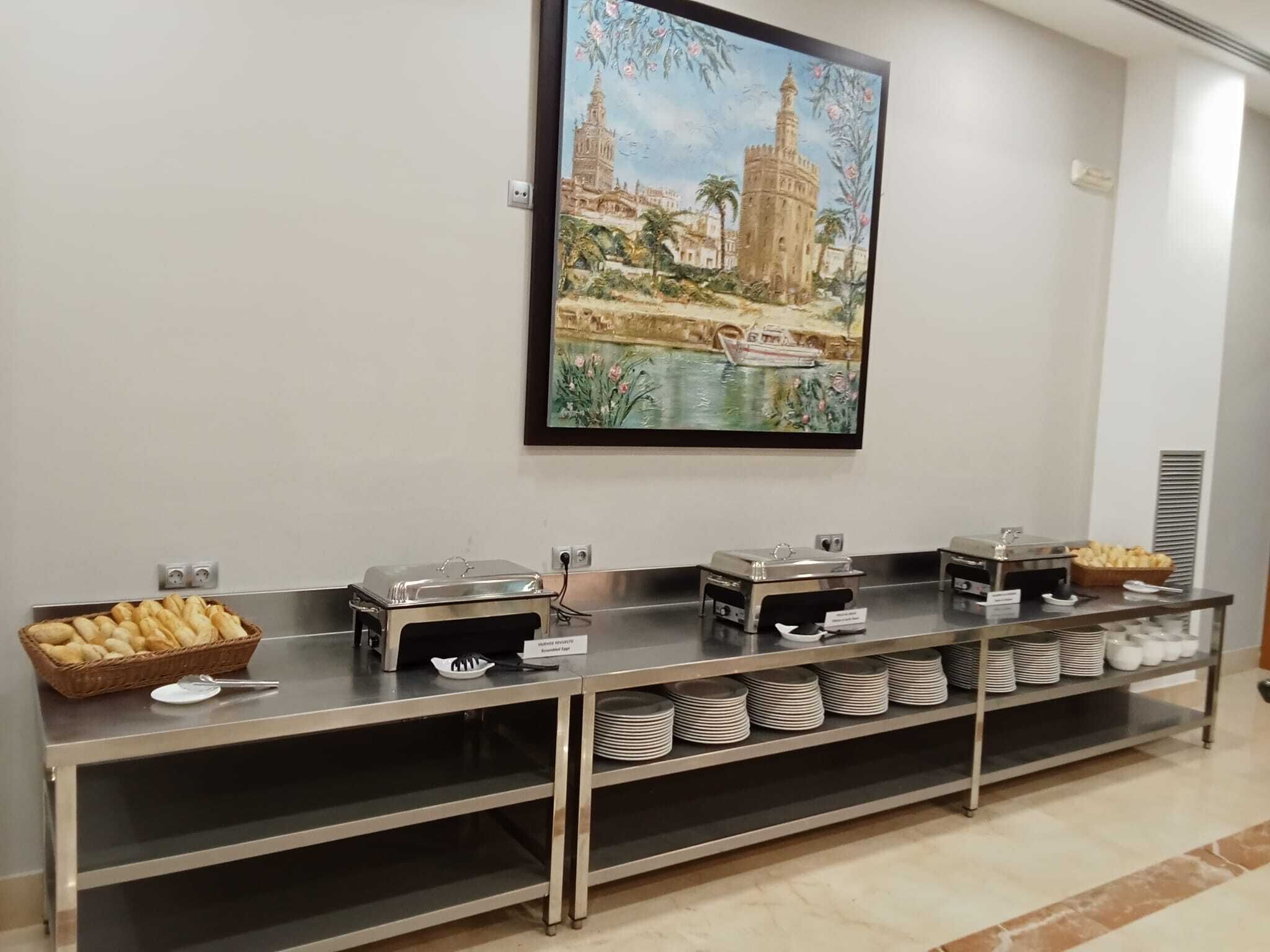 A buffet setup with various food items and a painting of a historic building on the wall.
