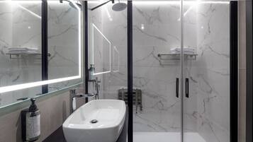 A modern bathroom with a glass-enclosed shower, a white sink, and a large mirror.