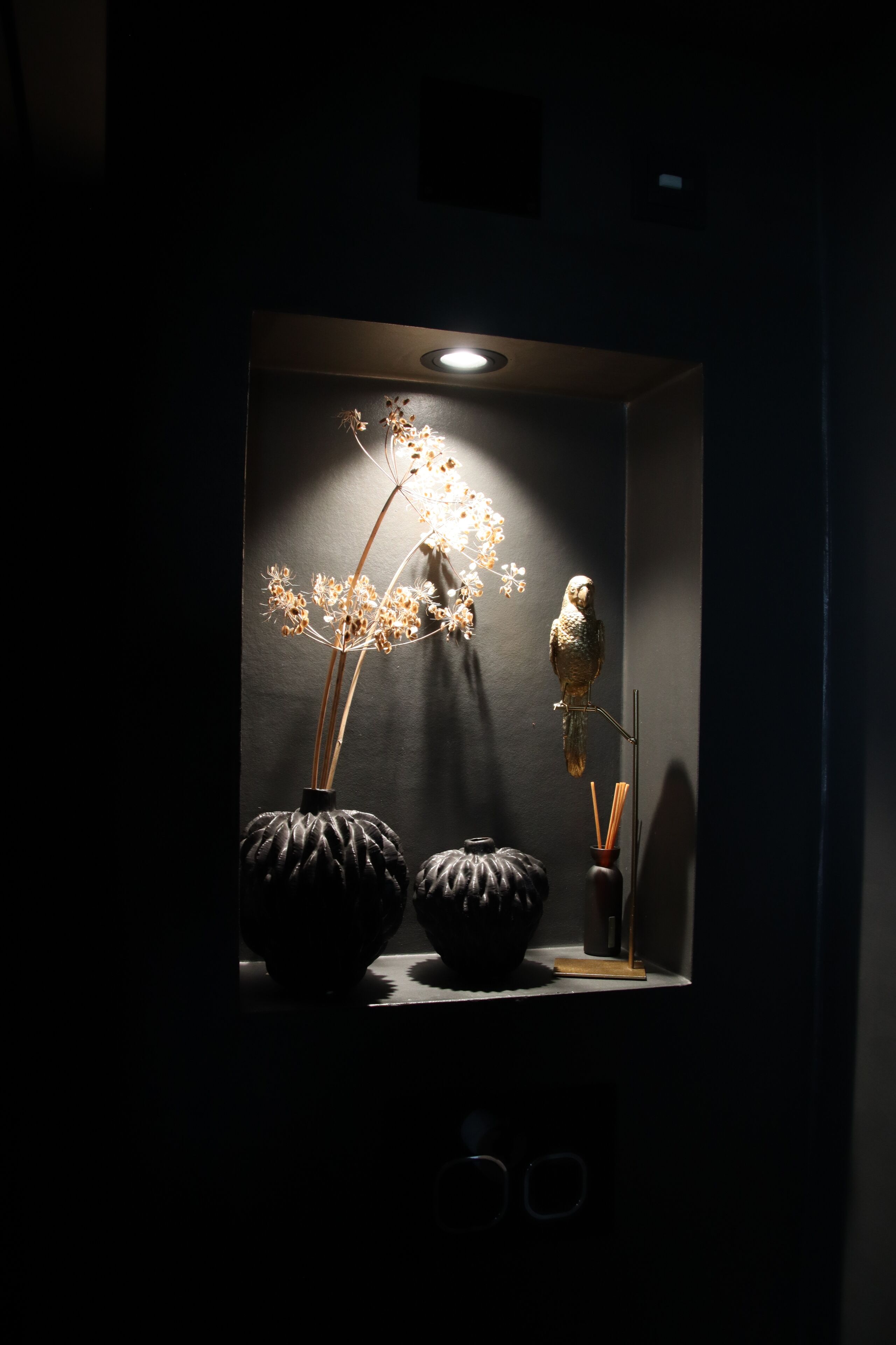 A dark room with a small shelf displaying a decorative bird, two vases, and a candle holder.