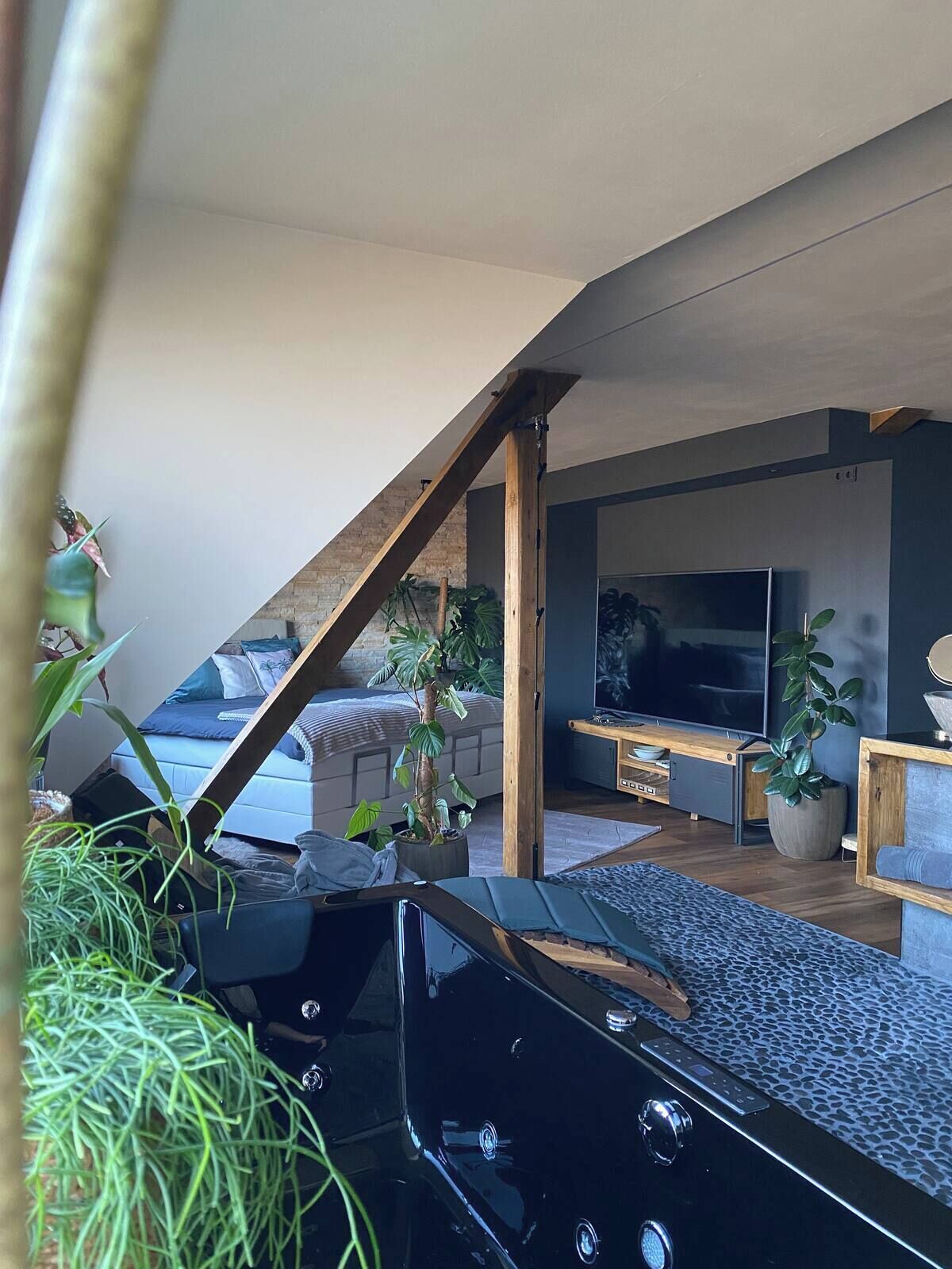 A modern loft bedroom with a sloped ceiling, a large bed, a TV, and a dining area with a wooden table and chairs.