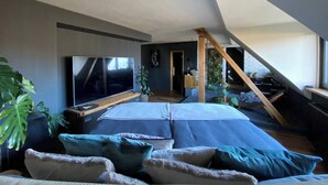 A modern loft bedroom with a large bed, a TV, and a staircase leading to an upper level. - Emerald Suite with whirlpool, sauna and massage chair (Essen)