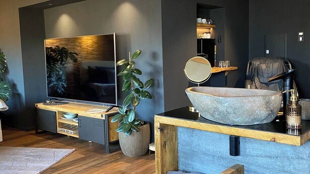 A modern living room with a large flat-screen TV, a stone bowl centerpiece, and a massage chair. - Emerald Suite with whirlpool, sauna and massage chair (Essen)