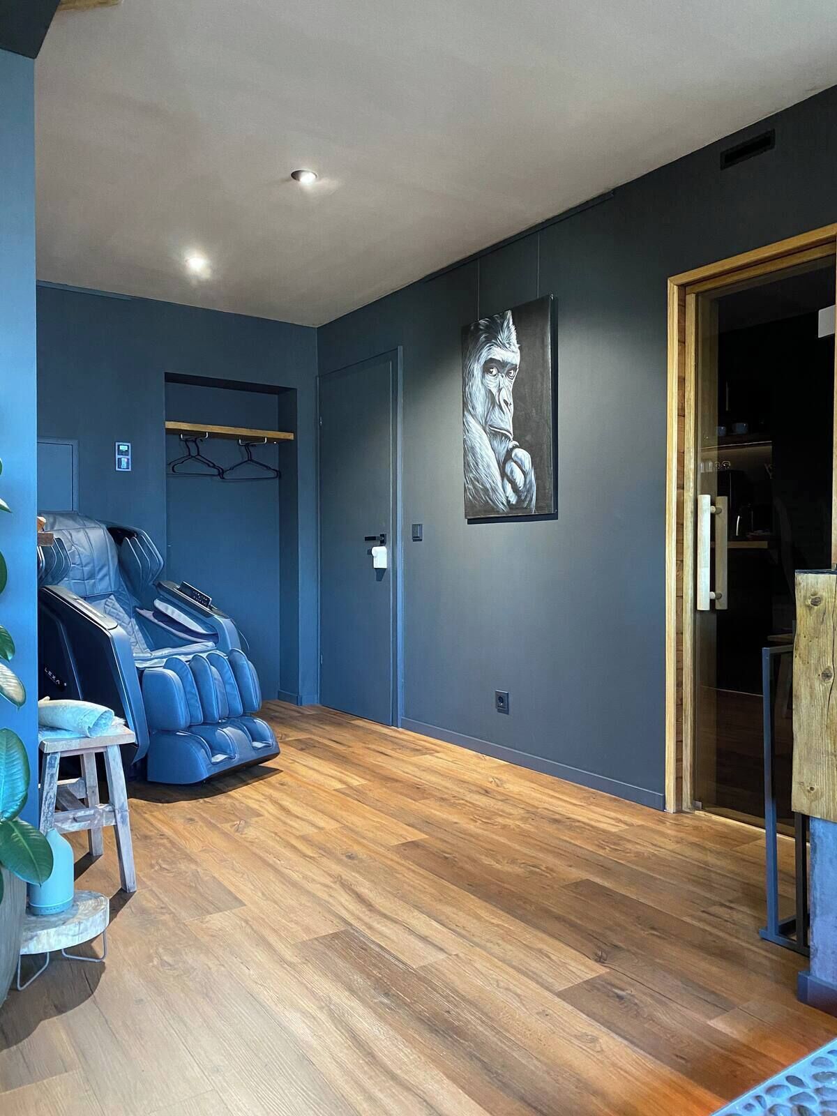 Quarto com cadeira de massagem, obra de arte na parede e piso de madeira.