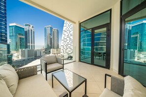 A modern balcony with a glass table, beige sofa, and city views.