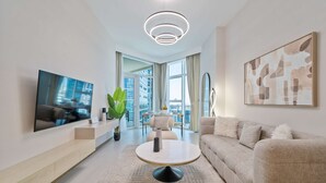 Una sala de estar moderna con un televisor de pantalla plana, una mesa redonda para café, un sofá y un ventanal con vistas a la ciudad.