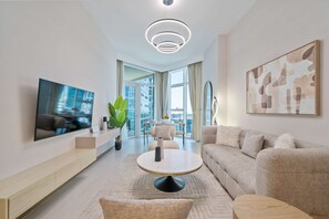 A modern living room with a flat-screen TV, a round coffee table, a sofa, and a large window offering a city view.