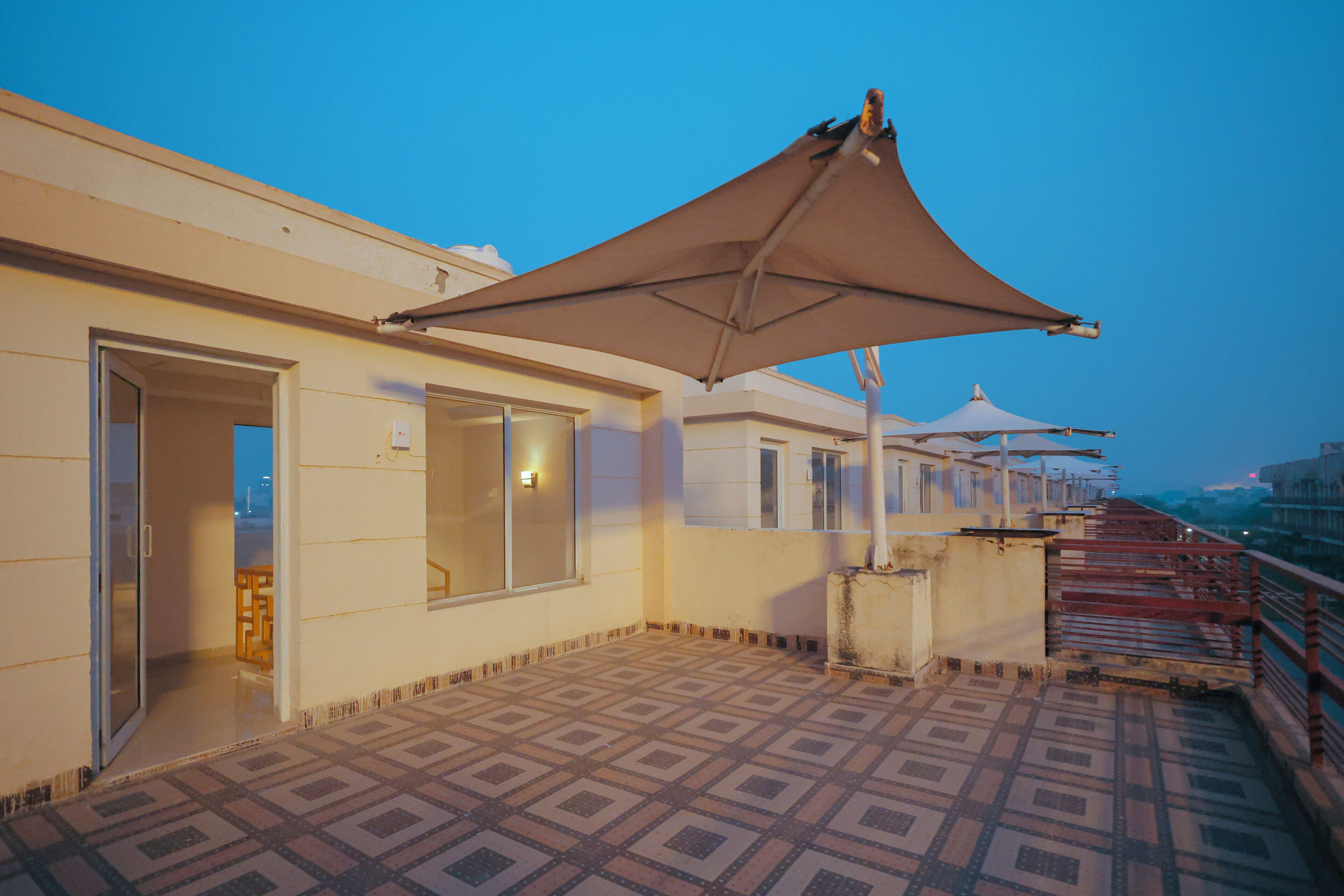 A rooftop terrace with patterned flooring, a large umbrella, and a view of the cityscape.