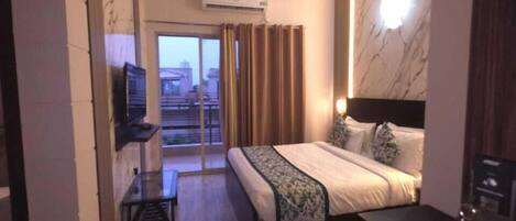 Habitación de hotel con cama, mesita de noche, televisor y balcón con cortinas.