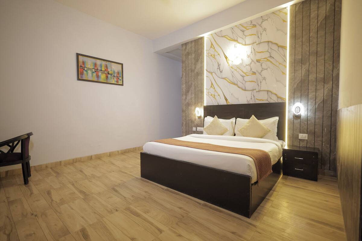A modern bedroom with a large bed, wooden flooring, a marble accent wall, and a painting on the wall.