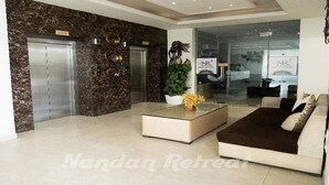 A modern lobby with a marble wall, a reception desk, a sofa, and an elevator.