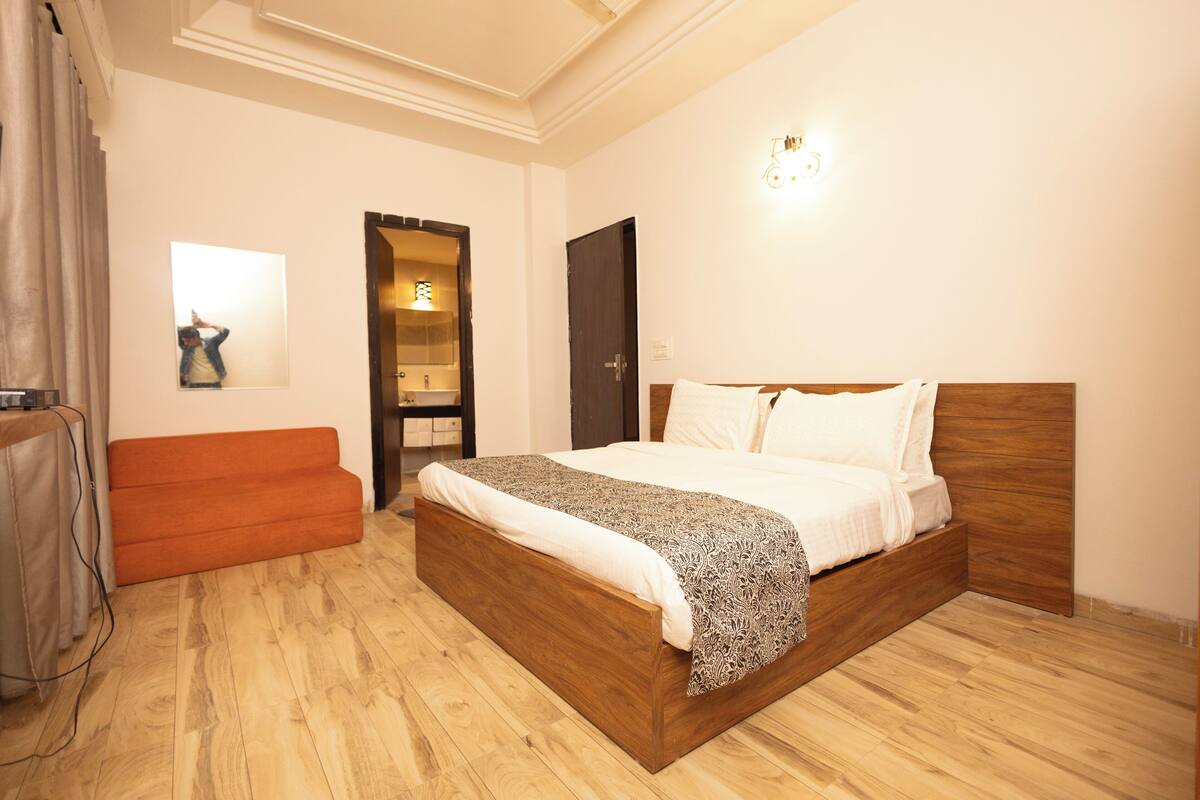 A hotel room with a wooden bed, a sofa, and a mirror on the wall.