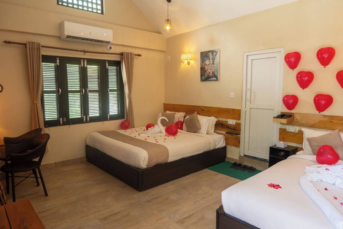A hotel room with a bed, a chair, a desk, a window with curtains, a door, and a wall with a picture.