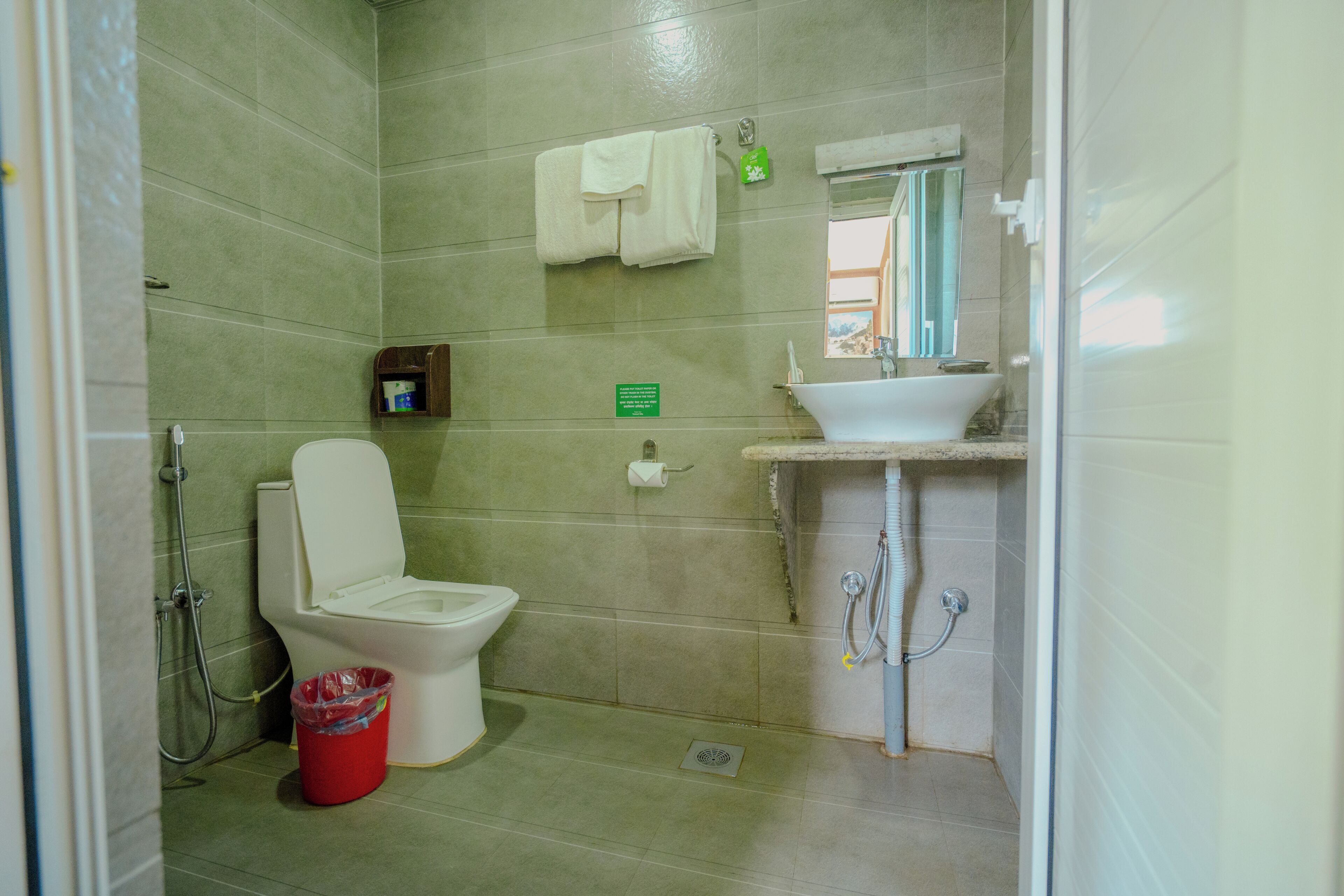 A bathroom with a toilet, sink, shower, and a red trash bin.