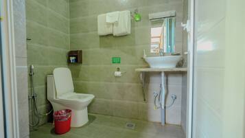 A bathroom with a toilet, sink, shower, and a red trash bin.