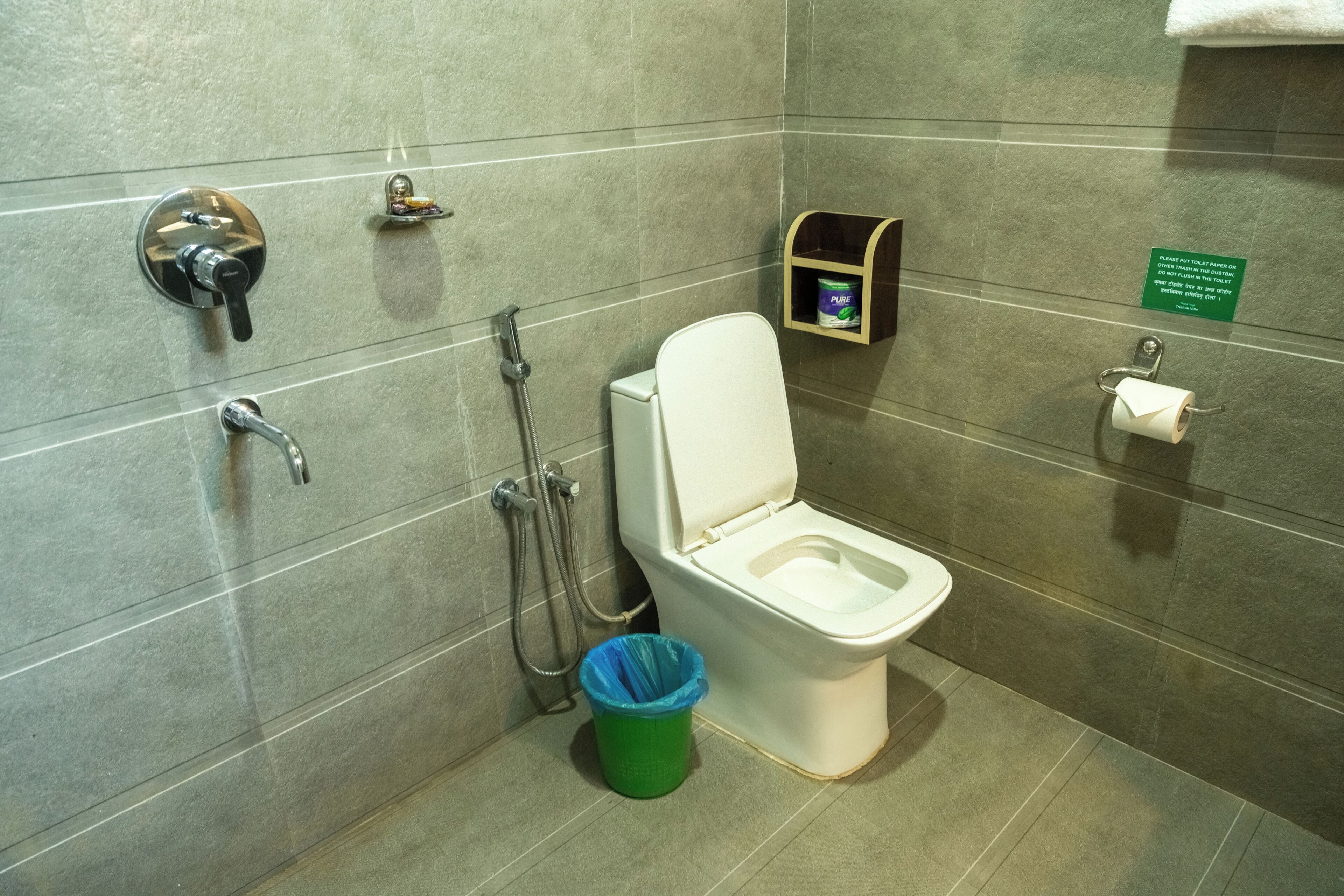A bathroom with a toilet, a shower, a trash bin, and a soap dispenser.