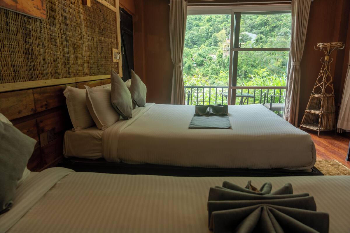 A hotel room with a large bed, a view of lush greenery through a window, and a woven wall decoration.