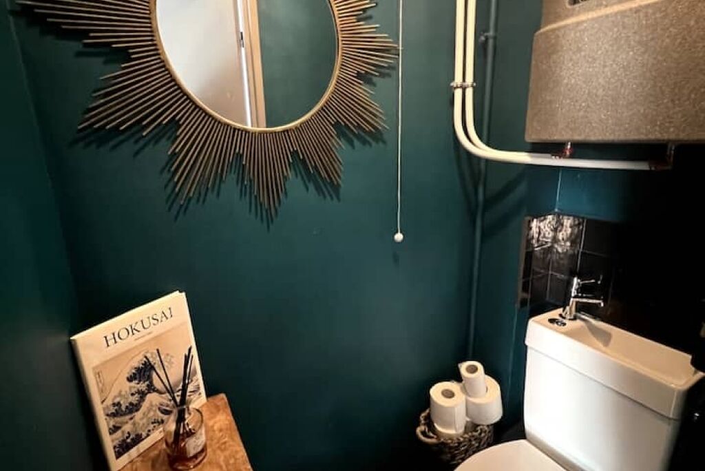 Een badkamer met toilet, wastafel en spiegel. Op een klein tafeltje ligt een boek getiteld 'HOKUSAI'.
