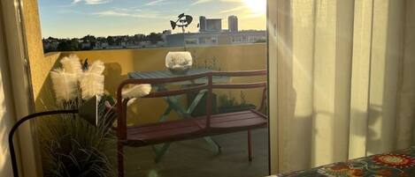 A balcony with a view of the city skyline, a metal chair, and a table with a decorative bowl.