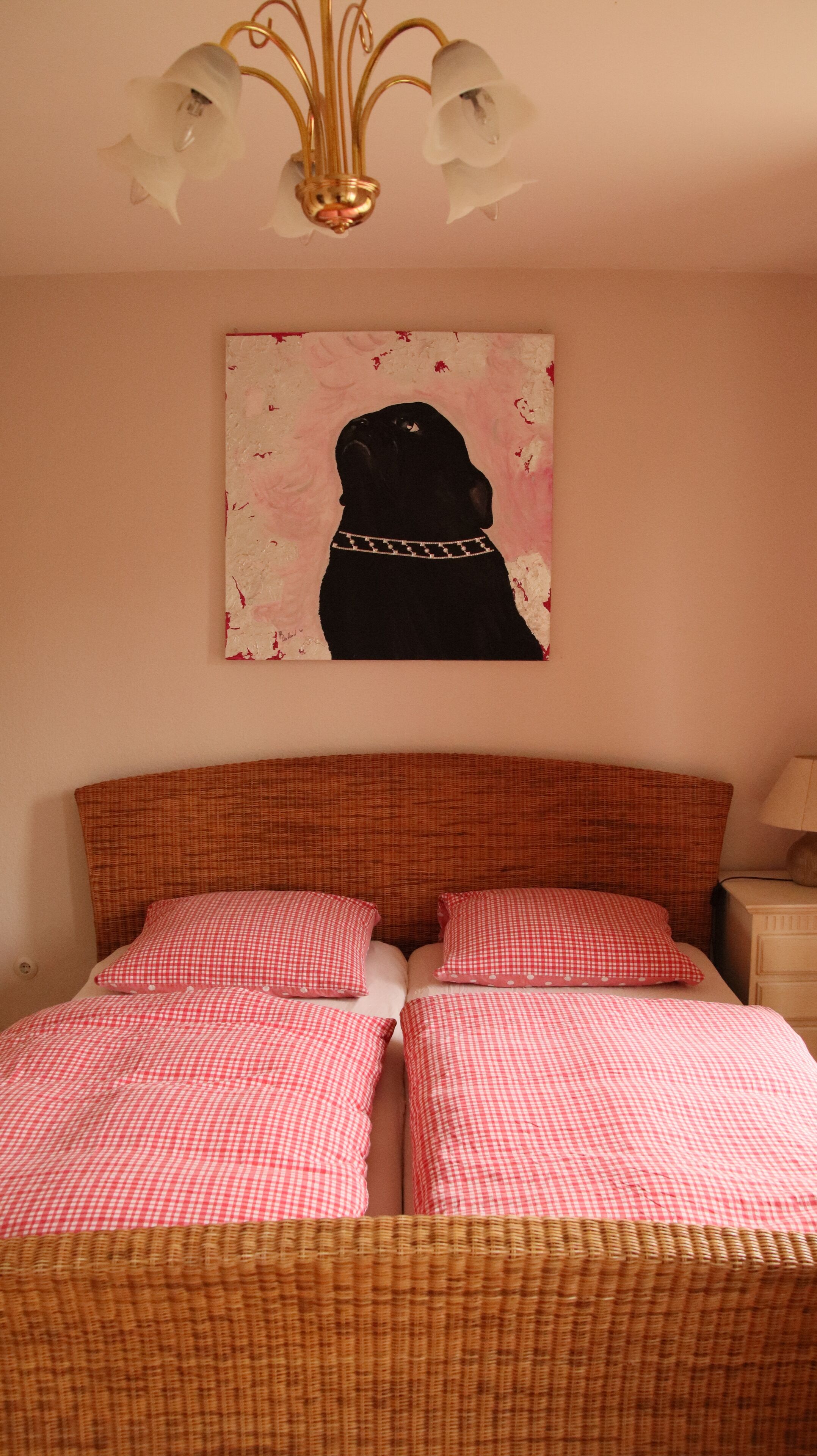 A bedroom with a bed featuring a checkered bedspread, a headboard, and a hanging artwork of a dog.