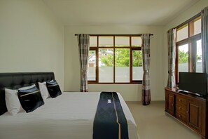 Une chambre à coucher avec un lit, des rideaux, un téléviseur posé sur un meuble en bois et une fenêtre donnant sur un paysage verdoyant.