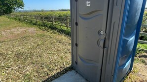 En transportabel toilet i et åbent marklandskab med en klar himmel.