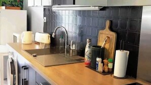 A kitchen with a modern design, featuring a stainless steel sink, a wooden cutting board, and various kitchen utensils.