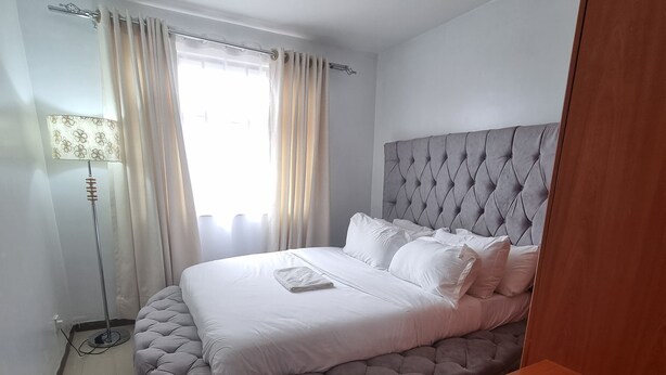 Een slaapkamer met een gestuwd hoofdeinde, een rond bed, wit beddengoed, een zacht vloerkleed en een vloerlamp.