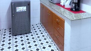 Een kleine keuken met een koelkast, magnetron, koffiezetapparaat en blender op het aanrecht.
