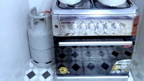 Een keuken met een fornuis, vier pannen met deksels en een gasfles.