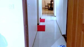 Een hal met een houten deurkozijn, een betegelde vloer en een rood tapijt dat leidt naar een eetgedeelte met een tafel en stoelen.
