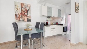 A modern kitchen with white cabinets, a glass dining table, and a painting on the wall. - Modern Seaside Apartment With Balcony - Erika (Tivat)