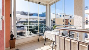 A balcony with a table and chairs, large windows, and a view of neighboring buildings. - Modern Seaside Apartment With Balcony - Erika (Tivat)