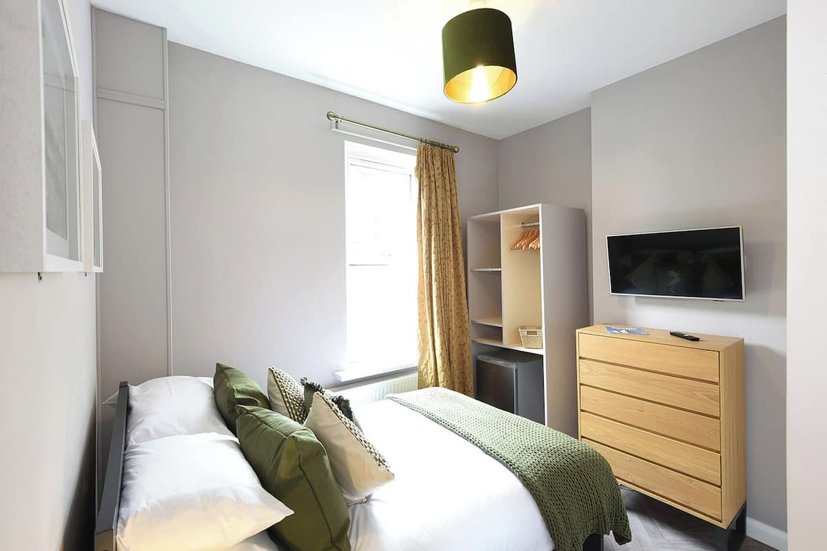 Un dormitorio moderno con una cama, un armario, un televisor y una ventana con cortinas.