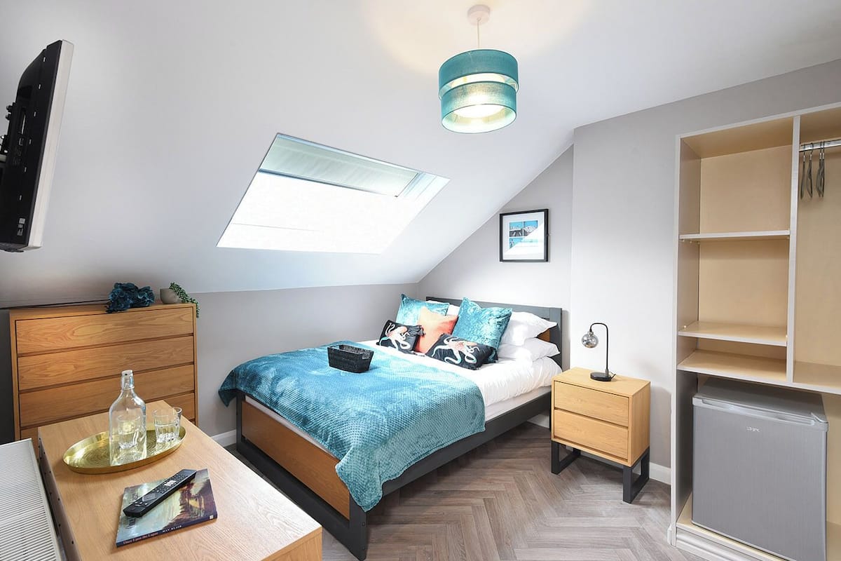 Un dormitorio con cama, mesitas de noche, escritorio, armario, tragaluz e iluminación en el techo.