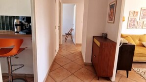 A kitchen with a coffee maker, a chair, and a dining area with a yellow sofa. - Large, modern, air-conditioned T4 (Montpellier)